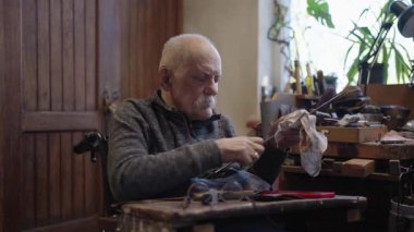 Senior gray haired male master in a wheelchair is working at his workshop sharpening japanese swords blade