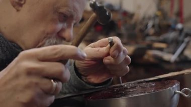 Tekerlekli sandalyede usta bir zanaatkar atölyesinde çalışıyor. Japon kılıcının ucuna çekiç ve keskiyle hormon resmi işliyor.