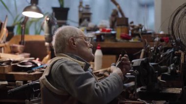 Tekerlekli sandalyedeki kıdemli yaşlı kuyumcu bir atölyede çalışıyor.