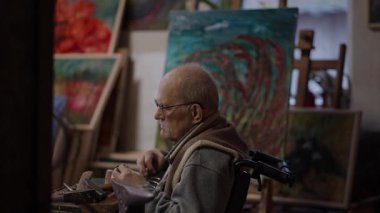 Senior elderly master jeweler in wheelchair works in a workshop with an anvil