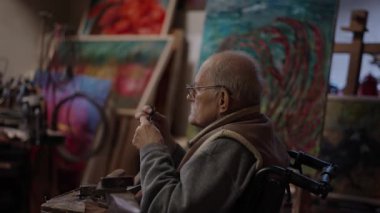Senior elderly master jeweler in wheelchair works in a workshop with an anvil