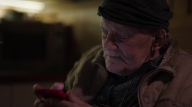 Tekerlekli sandalyede oturan yaşlı adam akıllı telefondan sosyal medyada kayıyor.