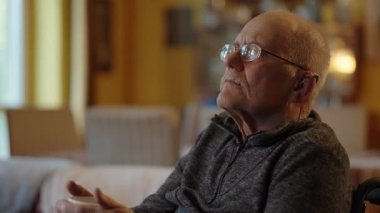 Tekerlekli sandalyede oturan yaşlı bir adam şöminenin yanında televizyon izliyor.