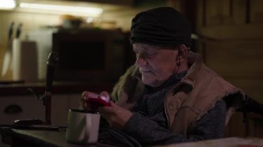 Tekerlekli sandalyede oturan yaşlı adam akıllı telefondan sosyal medyada kayıyor.