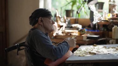 Tekerlekli sandalyedeki kıdemli sanatçı tuvaldeki yağlı boyaya altın sürüyor.