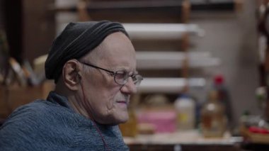 Evdeki atölyesinde tekerlekli sandalyede çalışan yaşlı bir zanaatkar.