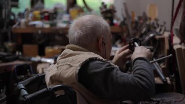 Evdeki atölyesinde tekerlekli sandalyede çalışan yaşlı bir zanaatkar.