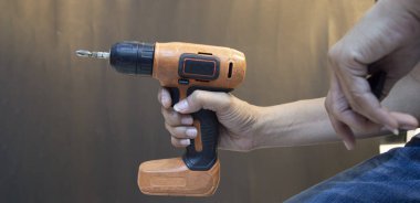 Elinde turuncu elektrikli tornavida tutan bir zanaatkar.