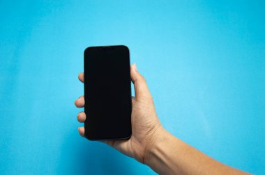 Mavi arka planda siyah bir akıllı telefon tutuyordu.