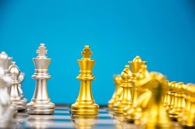 Gümüş satranç taşlarının önündeki altın kral satranç taşının çarpıcı görüntüsü satrançtaki strateji ve rekabeti sembolize ediyor..