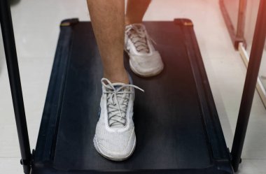 Asyalı bir adam koşu bandında koşmaya hazırlanıyor.