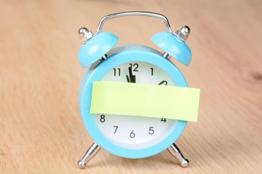 Adhesive note on a blue alarm clock on a wood background