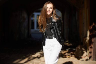 Siyah deri ceketli ve kotlu güzel bir kadın sokakta poz veriyor.