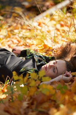 Sonbahar parkında yaprakları dökülmüş genç bir kız.