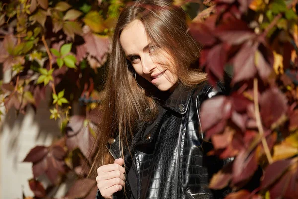 stock image portrait of smiling young woman in a black jacket on background of autumn leaves