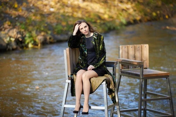 美丽的年轻女子坐在河边的椅子上 — 图库照片