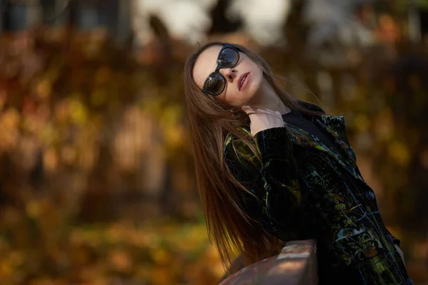 美丽的年轻女子 身穿绿色外套 戴着太阳镜 站在秋天的公园里 — 图库照片