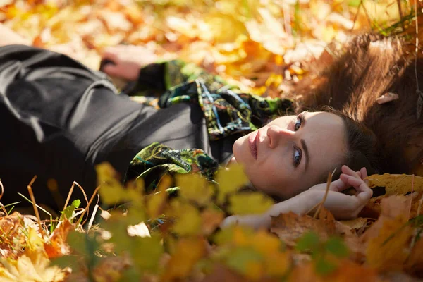 Sonbahar parkında yaprakları dökülmüş genç bir kız.