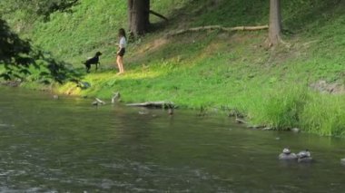Köpekli genç bir kız nehir kenarında yürüyor.