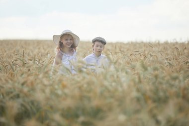 Buğday tarlasında duran şapkalı kız ve oğlanın portresi. 