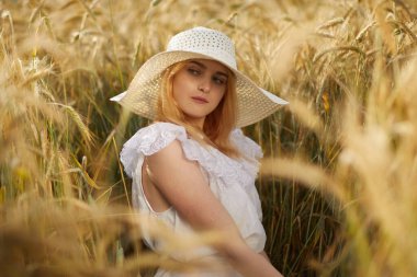 Buğday tarlasında kameraya poz veren şapkalı genç kadın portresi 