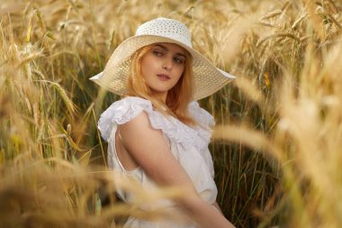 Buğday tarlasında kameraya poz veren şapkalı genç kadın portresi 