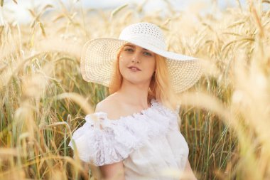 Gündüz vakti şapkalı ve buğday tarlasında oturan neşeli bir kadın.