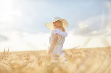 Buğday tarlasında gündüz poz veren şapkalı beyaz kadın.