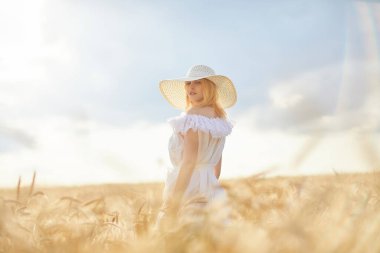 Buğday tarlasında gündüz poz veren şapkalı beyaz kadın.