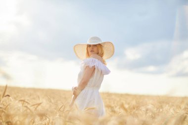 Buğday tarlasında gündüz poz veren şapkalı beyaz kadın.