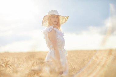 Buğday tarlasında gündüz poz veren şapkalı beyaz kadın.