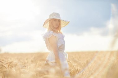 Buğday tarlasında gündüz poz veren şapkalı beyaz kadın.
