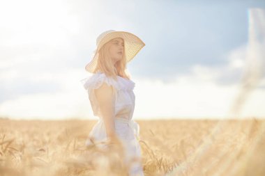 Buğday tarlasında gündüz poz veren şapkalı beyaz kadın.