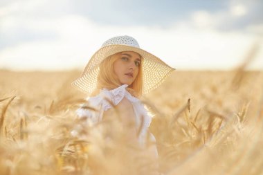 Şapkalı mutlu kadın portresi, buğday tarlasında poz veriyor. 