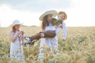 Anne ve çocuklar buğday tarlasında poz veriyorlar. 