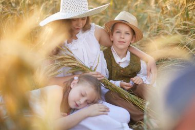 Anne ve çocuklar buğday tarlasında poz veriyorlar. 