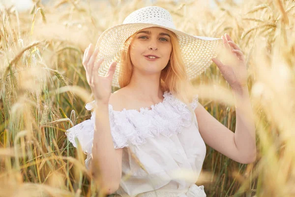 stock image cheerful woman wearing hat and sitting in wheat field during daytime