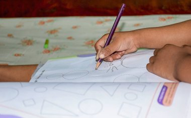 Back to school concept- a child drawing on some clouring book with oil pastle,creon colours as a  subject of study and school in natural environment not properly aranged.