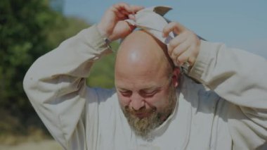 Arıcı kameraya gülümsüyor ve arı kovanının dışında koruyucu kaskını takıyor.