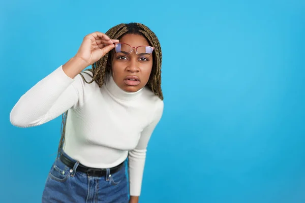 Studio portrait with blue background of an african woman with eyeglasses staring at camera in disbelief
