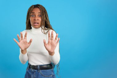 Avuç içleri titreyen korkmuş bir afro kadının mavi arka planlı stüdyo portresi.