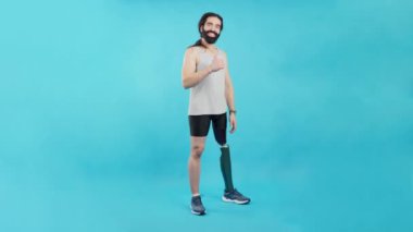 Stüdyo portresi mavi arka planda ve bacağında protezi olan bir adamın fotokopi odası kameraya gülümseyen ve başparmağıyla iyi olması için işaret eden.