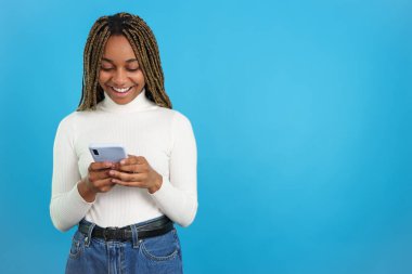 Cep telefonunu kullanan mutlu bir Afrikalı kadının mavi arka planlı stüdyo portresi.