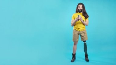 Mavi arkaplanı olan bir stüdyo portresi ve protez bacağı ve cep telefonu olan havalı bir adamın mekânının kopyası.