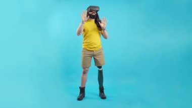 Studio portrait with blue background and copy space of a man with prosthetic leg gesturing while using a virtual goggles