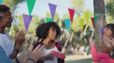 Multiethnic friends clapping and singing Happy Birthday in a park