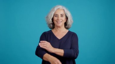 Studio video with blue background of a proud mature woman looking at camera with arms crossed