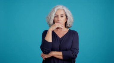 Studio video with blue background of an aged woman gesturing and looking up with thoughtful expression
