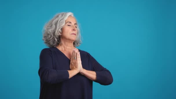 工作室的蓝色背景视频 一个成熟的女人双手交叉祈祷时抬起头看 — 图库视频影像