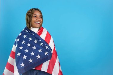 Studio portrait with blue background of an african woman looking happily to one side wrapped in a North American flag